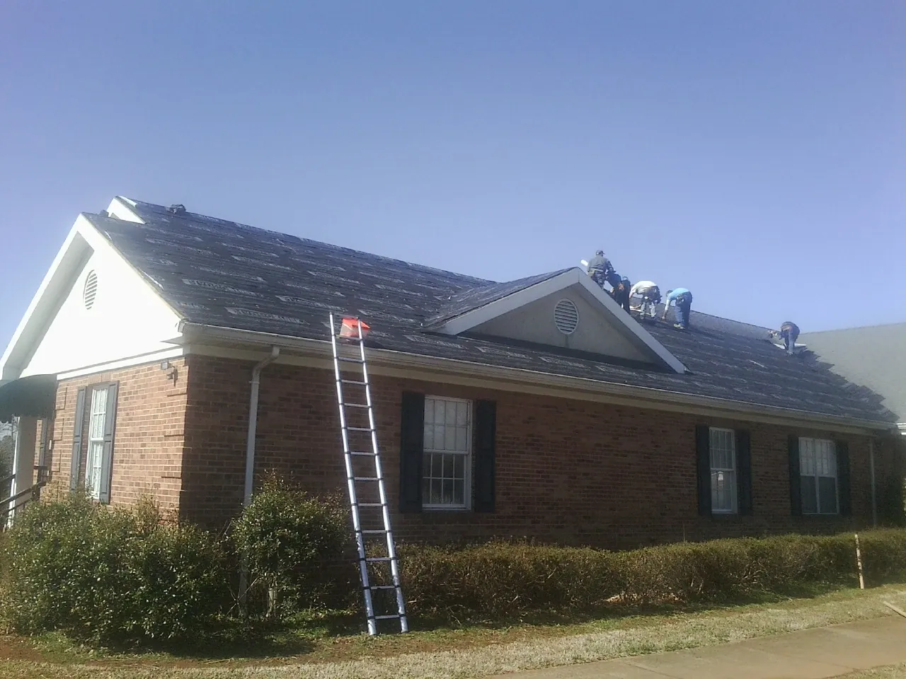 Crew tearing shingles off a brick ranch roof with a ladder set — Emergency Roof Repair work by our crew in Downers Grove