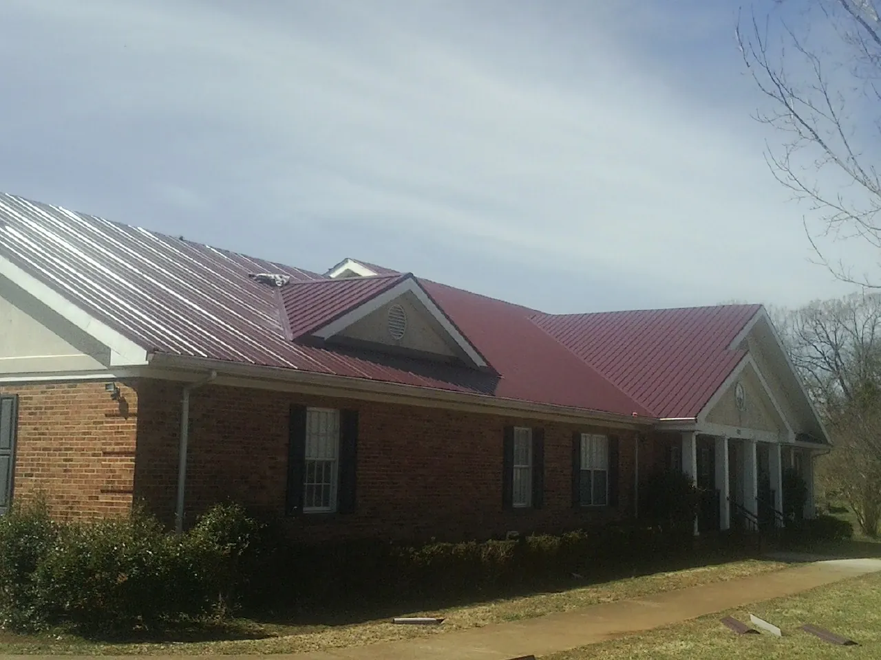 Red metal roof with gabled entries on a long brick building, from a Hail Damage Roof Repair job in Downers Grove