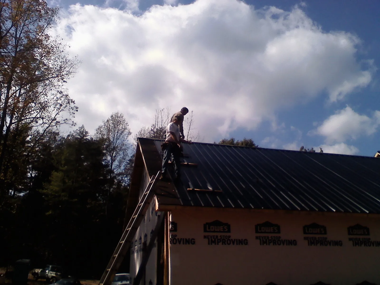 Roofer fastening dark metal panels high against a cloudy sky, from a Roof Inspection job in Downers Grove