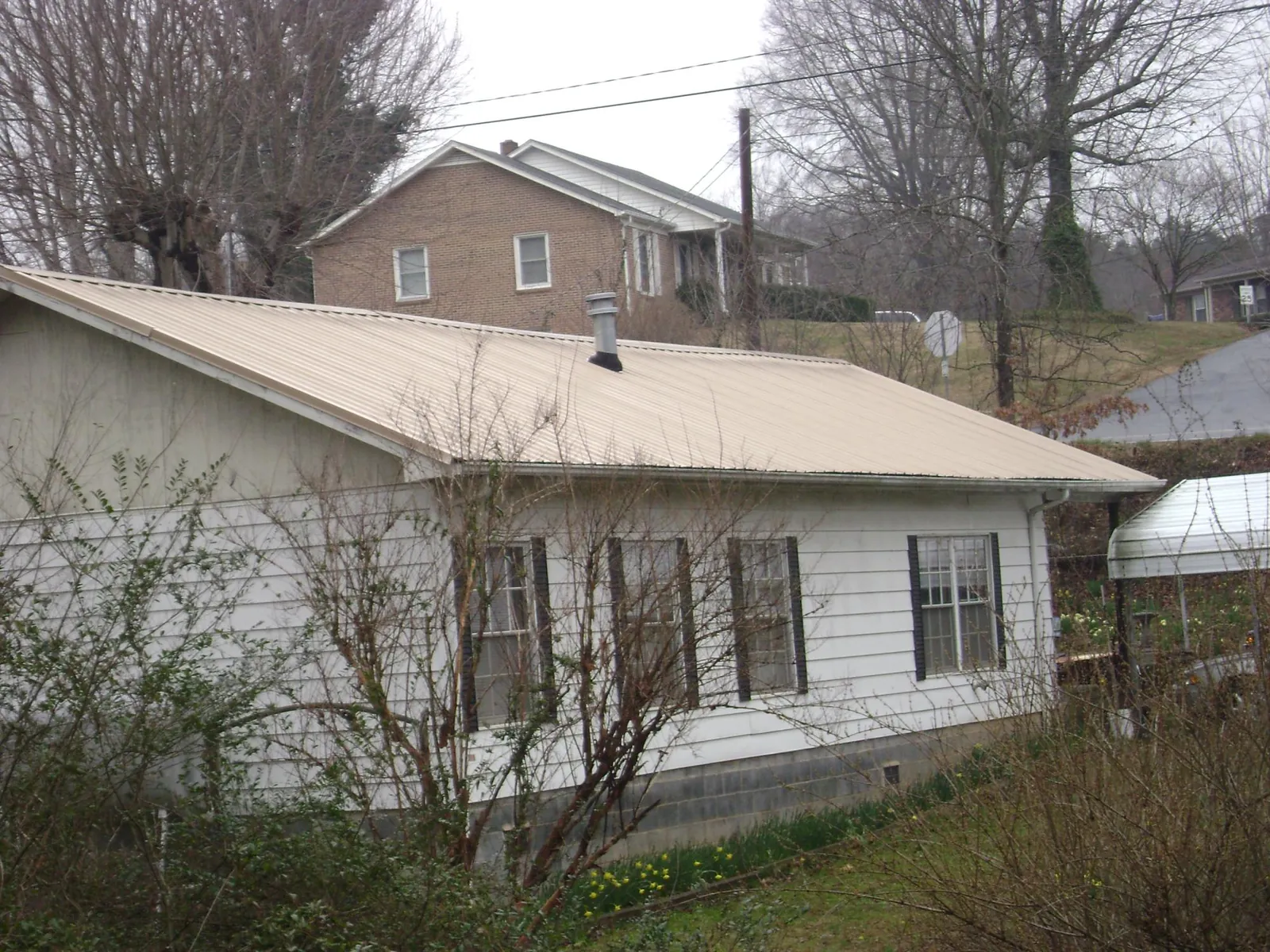 Tan metal roof on a white sided house set into a hillside — Commercial Roofing by Roofing Brothers in Downers Grove