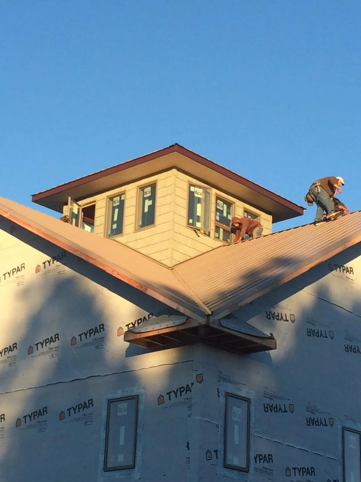 Roofers working around a rooftop cupola on a new metal roof at sunset — Roof Waterproofing in Downers Grove by Roofing Brothers